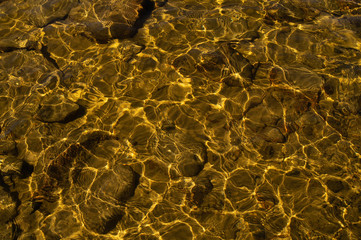 Shiny transparent water. clear water with pebbles and stone on the bottom. shining reflections of sun rays and ripples on the water