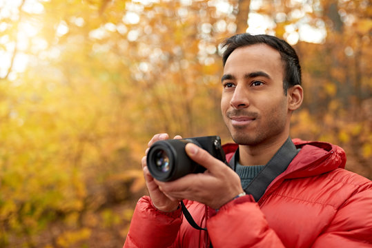 Attractive indian man taking pictures with a mirrorless camera through the forest in the fall in Canada