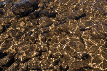Shiny transparent water. clear water with pebbles and stone on the bottom. shining reflections of sun rays and ripples on the water
