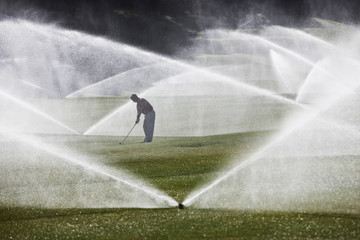 Golfer playing golf on golf course during sprinkler system turns on