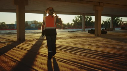 Inside of the Commercial / Industrial Building Construction Site: Engineer Surveyor Finishes Day's Job Carries Tripod Theodolite and Walks into Sunset