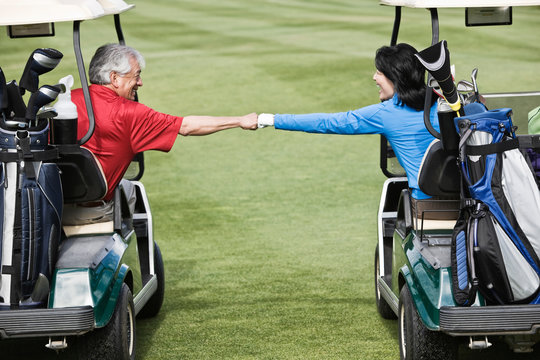 Senior friends doing fist bump between golf carts