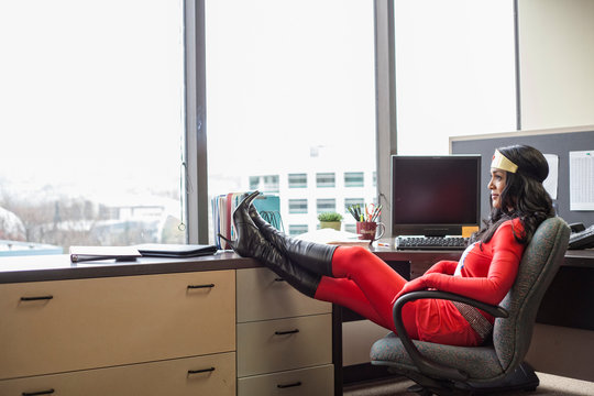 Businesswoman In Super Hero Costume Sitting In Office