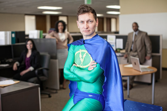 Portrait of businessman in super hero costume with colleagues in background