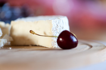Camembert from goat's milk cut into slices on a wooden board still life with sweet cherry berries close-up