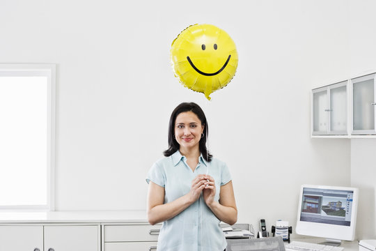 Portrait of smiling woman holding smiley face balloon in office
