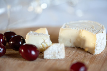 Camembert from goat's milk cut into slices on a wooden board still life with sweet cherry berries. With a clear glass lying on the plan is out of focus