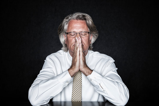 Man with eyes closed sitting at table in prayer pose