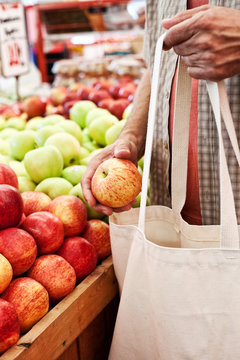 Man with shopping bag holding apple in market