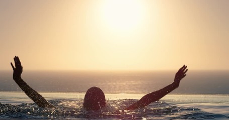 woman jumping out of swimming pool with arms raised enjoying summer vacation in mediterranean hotel resort with view of ocean at sunset travel freedom silhouette 4k