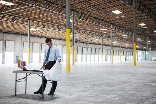 Architect Looking At Blueprint While Standing In Warehouse