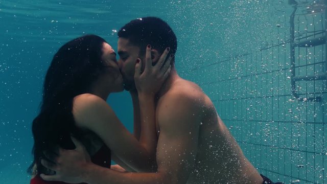 young couple kissing underwater in swimming pool enjoying intimate kiss romantic lovers submerged in water floating with bubbles in passionate intimacy 