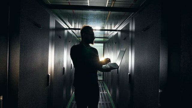 Silhouette of an IT worker with a laptop in the dark server unit. IT Engineer working in a server room.