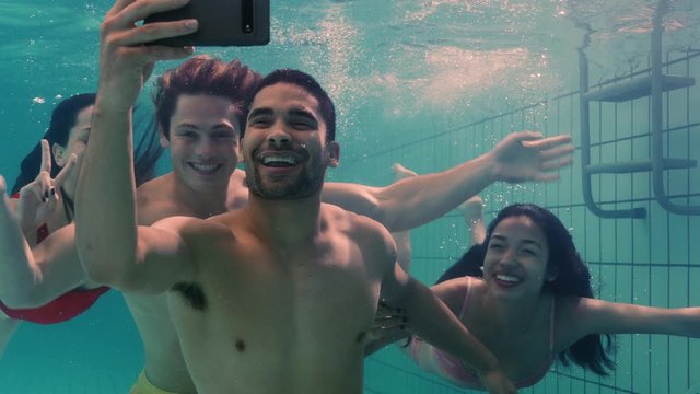 cool friends taking photo underwater using smartphone in swimming pool having fun swim submerged in clear water