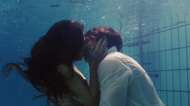 romantic couple kissing underwater in swimming pool wearing clothes young people in love enjoying intimate kiss lovers submerged in water floating with bubbles in passionate intimacy 
