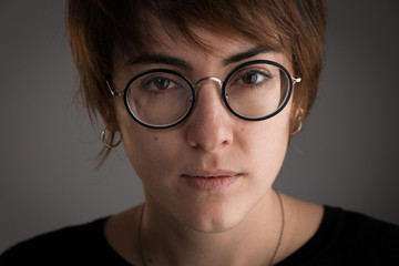 Close-up of girl with brown short hair and glasses looking at the camera with serious expression