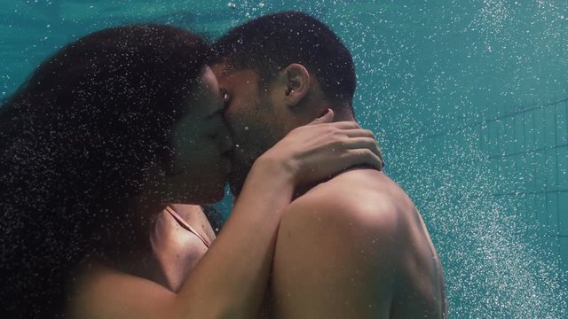 young couple kissing underwater in swimming pool enjoying intimate kiss romantic lovers submerged in water floating with bubbles in passionate intimacy 