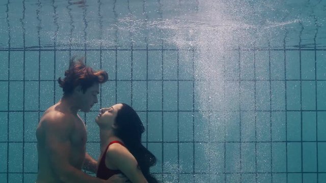 underwater couple kissing in swimming pool young people in love enjoying romantic kiss passionate lovers submerged in water floating with bubbles in playful intimacy 