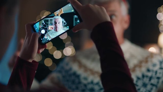 christmas funny grandfather wearing reindeer antlers posing for granddaughter taking photos using smartphone having fun laughing at silly grandpa enjoying festive holiday celebration at home 4k 