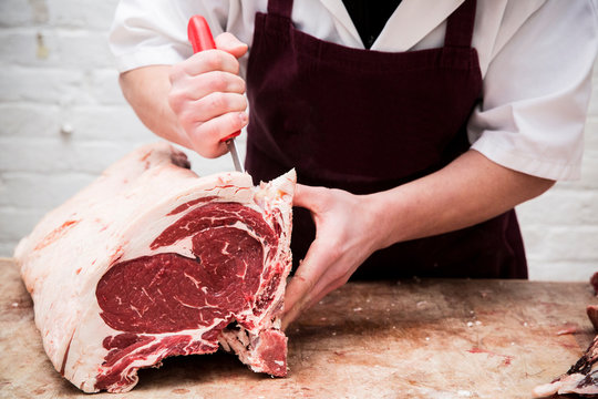 Midsection of butcher chopping beef forerib with knife