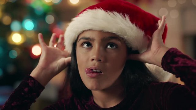 portrait little hispanic girl celebrating christmas wearing hat making faces enjoying festive holiday with colorful lights having fun evening at home 4k footage 