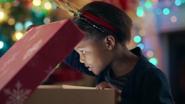 happy african american girl unwrapping christmas present looking in box with glow on face surprised child excited for special gift having fun enjoying festive holiday celebration 4k