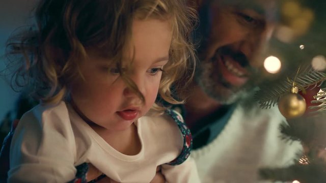little girl with father decorating christmas tree with beautiful ornaments and baubles child helping dad hang festive decorations at home on calm evening 4k footage