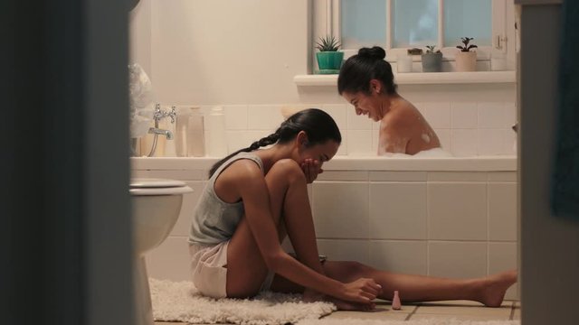 happy teenage sisters chatting in bathroom young girl bathing with sister sitting next to bath having conversation sharing gossip siblings enjoying quality time together at home 4k