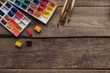top view of watercolor paint palettes and paintbrushes on wooden surface with copy space