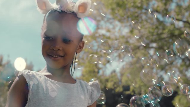 little african american girl playing with soap bubbles blowing playfully cute child having fun summer day playing bubble popping game in park 4k