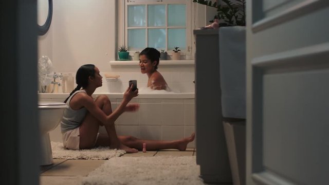 happy teenage sisters chatting in bathroom young girl bathing with sister sitting next to bath having conversation sharing gossip siblings enjoying quality time together at home 4k