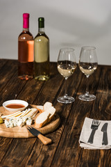 bottles of wine, wine glasses, cutlery, cheese, olives, sauce and bread on wooden surface