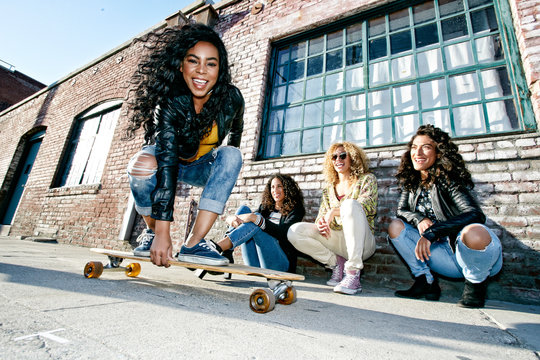 Women looking at their friend skateboarding on sidewalk