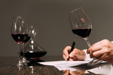 partial view of sommelier writing at table and holding wine glass
