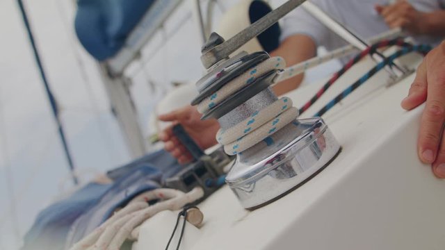 Hand pulls the winch close up. Rope of marine equipment on sailing vessel. Sailor pulling out main sail with blue striped rope the yacht. Sea tourism and Atlantic lifestyle Shot URSA 4.6K