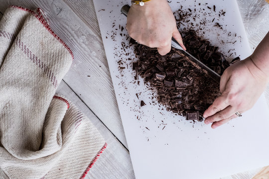 Overhead View Of Woman's Hand Chopping Chocolate Pieces With Cleaver