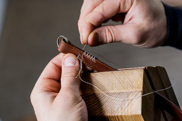 Close up of craftsman stitching pieces of leather in clamp