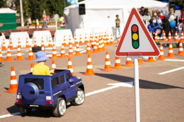 Child on an electric car. Children's cars in a city park. A child enjoys driving a car. Special area for racing on small cars. Fun for kids.