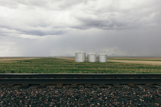 Stormy clouds over grain silos on farmland with rail track in foreground
