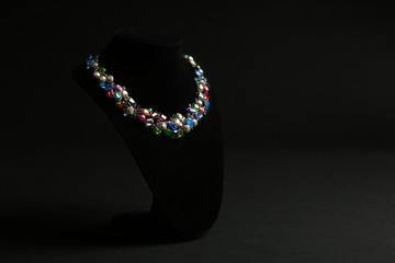 Elegant necklace on stand against black background, space for text. Luxury jewelry