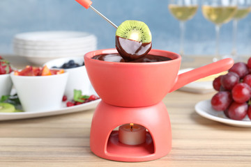 Dipping kiwi slice into pot with chocolate fondue on table