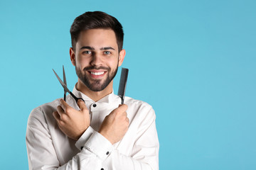 Young hairstylist holding professional scissors and comb on color background, space for text
