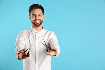 Fototapeta premium Young hairstylist holding professional scissors on color background, space for text