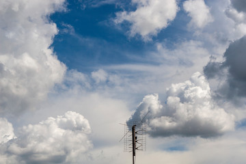 Obraz premium An old television antenna against a background of white clouds running across the sky. How to catch a television antenna signal. Meteo phenomenon in the atmosphere.