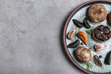 Plate with black garlic on grey table, top view. Space for text