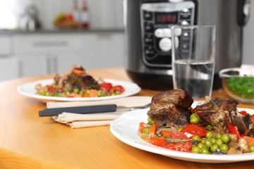 Plate with meat and garnish prepared in multi cooker on wooden table in kitchen. Space for text