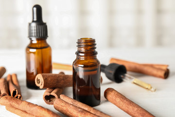 Bottles of essential oils and cinnamon sticks on white wooden table