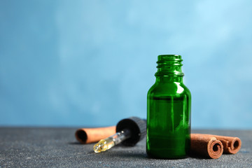 Bottle of essential oil and cinnamon sticks on table against blue background. Space for text