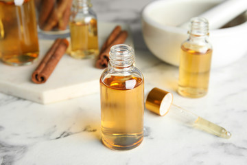 Bottles with cinnamon essential oil on marble table