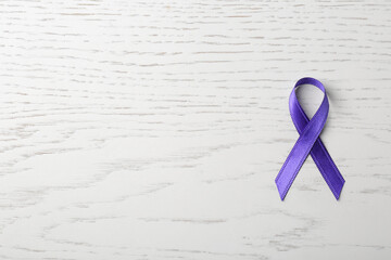 Purple ribbon on white wooden background, top view with space for text. Domestic violence awareness